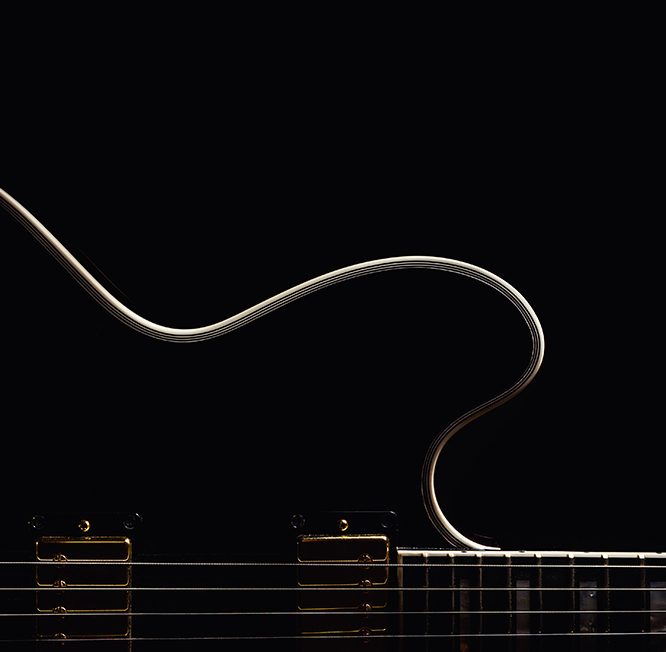 Close-up of a jazz guitar's body and strings in low light, highlighting its elegant curves and golden hardware.