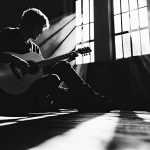 Kelly Joe Phelps playing an acoustic guitar on stage during a live jazz performance, with a spotlight highlighting his focused expression.